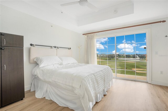 bedroom featuring ceiling fan, a raised ceiling, light wood-type flooring, and access to outside