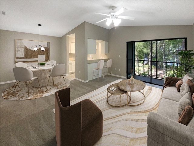 carpeted living room with ceiling fan with notable chandelier and vaulted ceiling