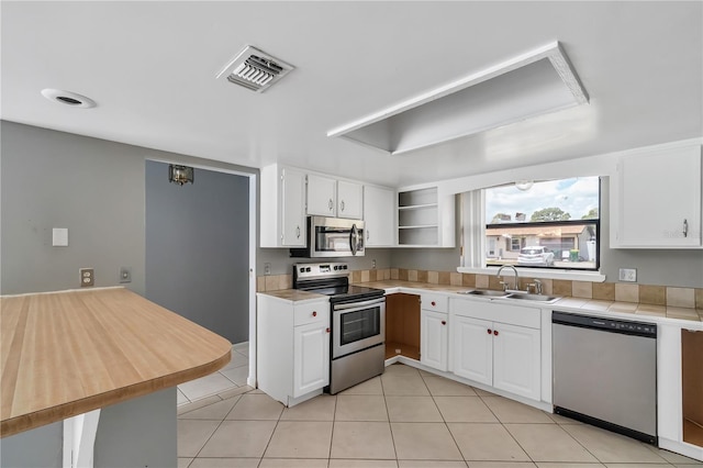 kitchen with appliances with stainless steel finishes, light tile floors, sink, white cabinets, and tile countertops