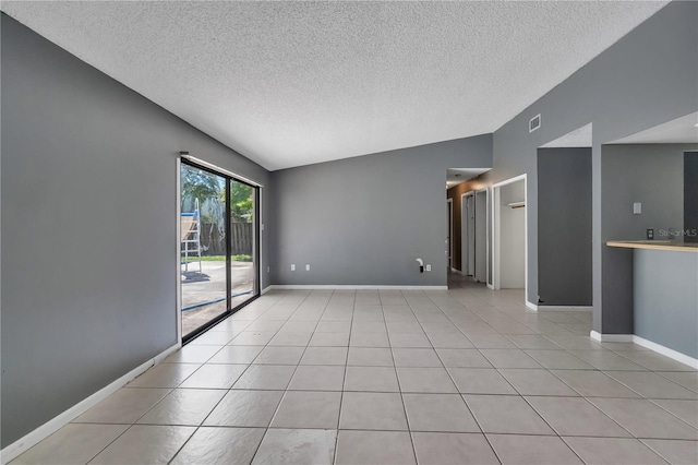 spare room featuring a textured ceiling, lofted ceiling, and light tile flooring