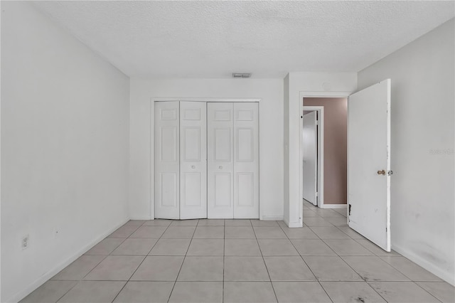 unfurnished bedroom featuring a textured ceiling, a closet, and light tile floors