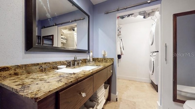 bathroom with stacked washer / dryer, tile flooring, vanity, and toilet