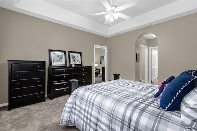 carpeted bedroom with ceiling fan and a raised ceiling