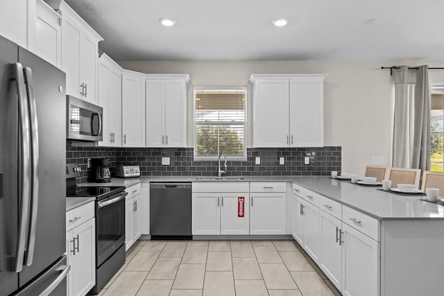 kitchen with kitchen peninsula, backsplash, appliances with stainless steel finishes, sink, and light tile floors