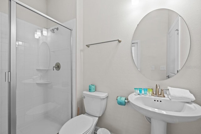 bathroom featuring a shower with shower door, sink, and toilet