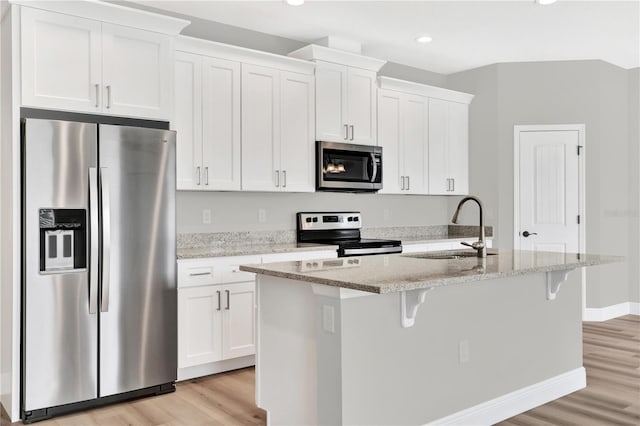 kitchen featuring appliances with stainless steel finishes, sink, white cabinetry, light stone countertops, and a kitchen island with sink