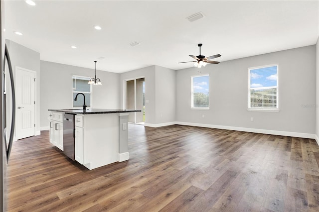 kitchen with hardwood / wood-style floors, an island with sink, dishwasher, ceiling fan with notable chandelier, and white cabinetry