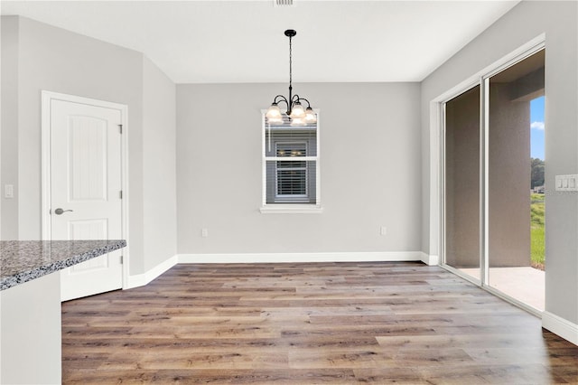 unfurnished dining area featuring a notable chandelier, a healthy amount of sunlight, and hardwood / wood-style floors