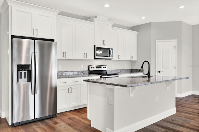 kitchen with appliances with stainless steel finishes, white cabinetry, an island with sink, and dark hardwood / wood-style flooring