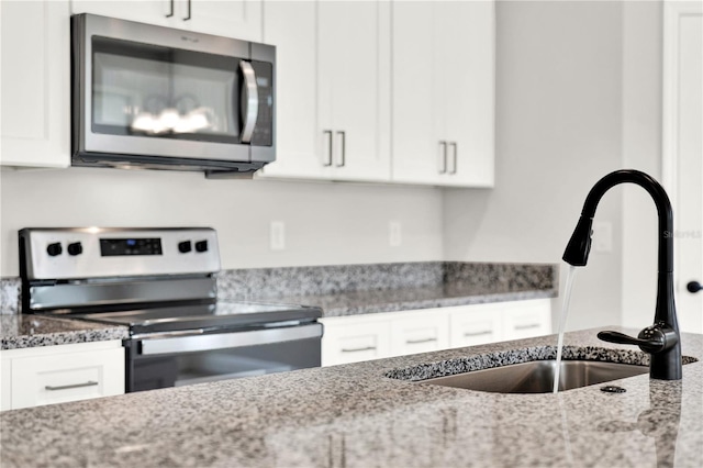 kitchen featuring appliances with stainless steel finishes, white cabinetry, sink, and light stone countertops