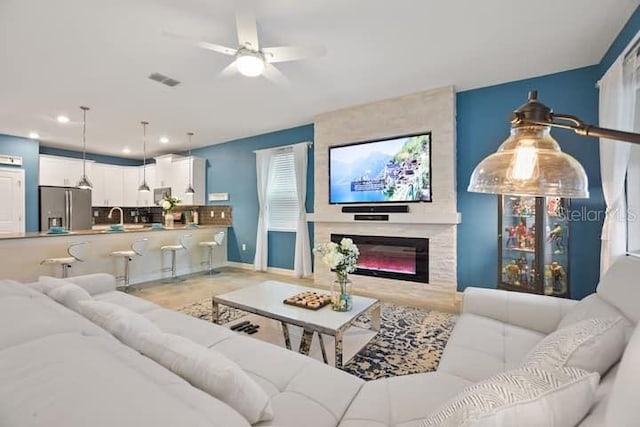 living room featuring a large fireplace, sink, and ceiling fan