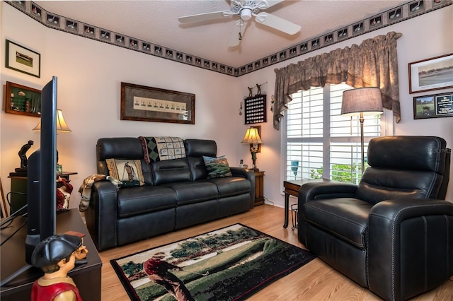 living room featuring ceiling fan, light hardwood / wood-style flooring, and a textured ceiling