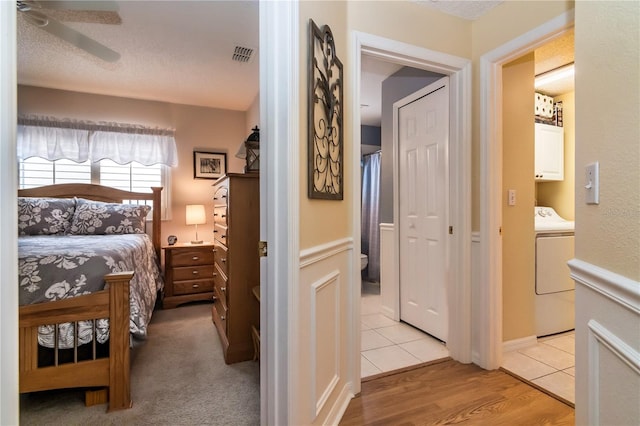 bedroom with light carpet, a textured ceiling, ceiling fan, and washer / clothes dryer