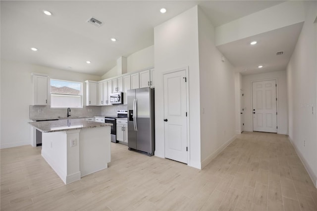 kitchen featuring white cabinets, a kitchen island, stainless steel appliances, sink, and light stone counters