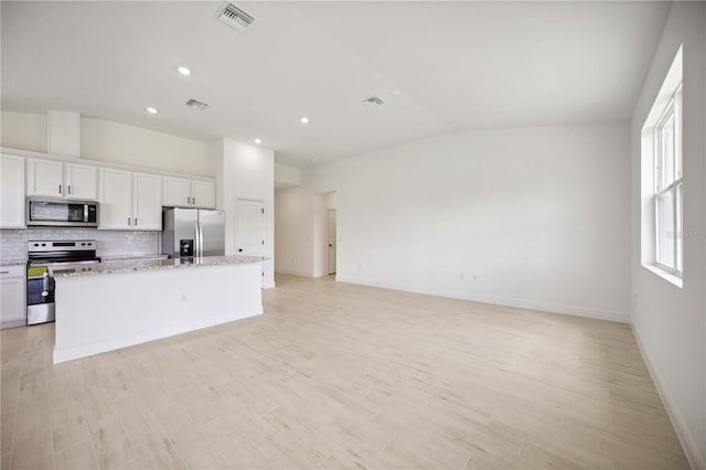 kitchen featuring white cabinetry, an island with sink, appliances with stainless steel finishes, lofted ceiling, and light stone countertops