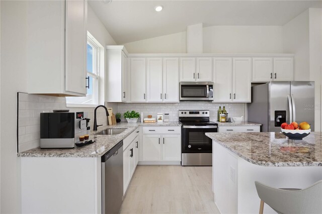 kitchen featuring white cabinetry, appliances with stainless steel finishes, lofted ceiling, light stone counters, and sink