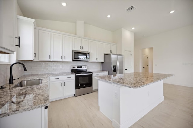 kitchen with a center island, sink, light stone countertops, appliances with stainless steel finishes, and white cabinets