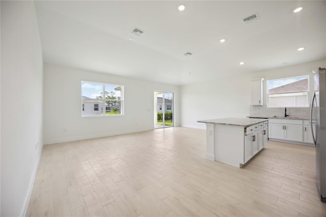 kitchen with light stone countertops, a kitchen island, white cabinetry, tasteful backsplash, and sink