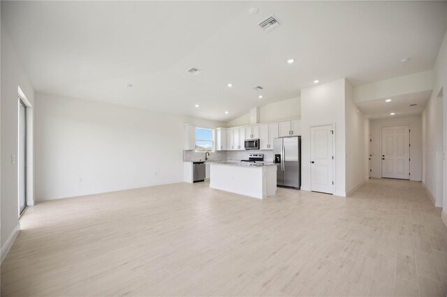 kitchen with white cabinets, appliances with stainless steel finishes, a center island, vaulted ceiling, and light wood-type flooring