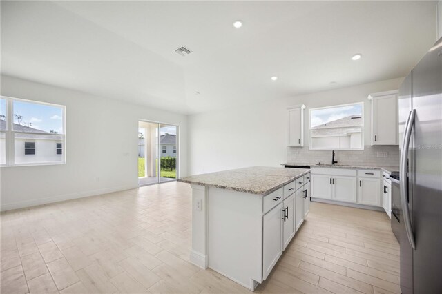 kitchen with sink, white cabinetry, stainless steel fridge, and a kitchen island