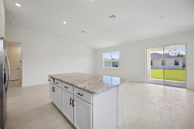 kitchen featuring vaulted ceiling, a center island, light stone countertops, stainless steel fridge with ice dispenser, and white cabinets