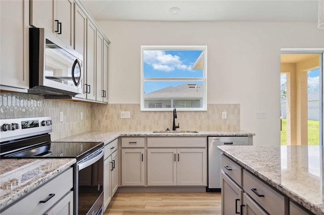 kitchen with sink, appliances with stainless steel finishes, light stone countertops, light hardwood / wood-style floors, and decorative backsplash