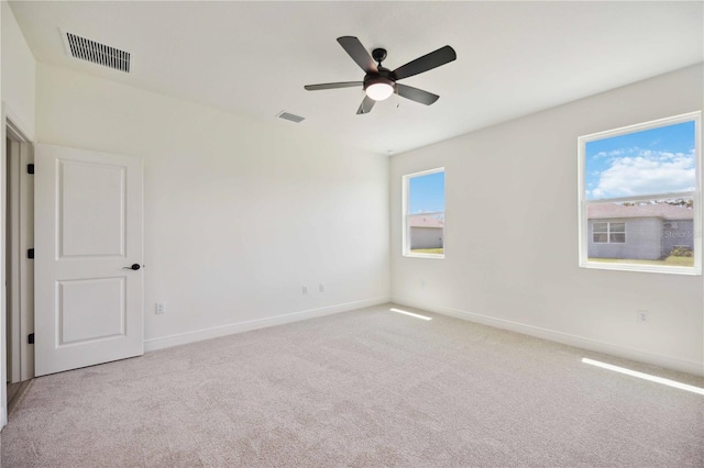 empty room with ceiling fan, light colored carpet, and plenty of natural light