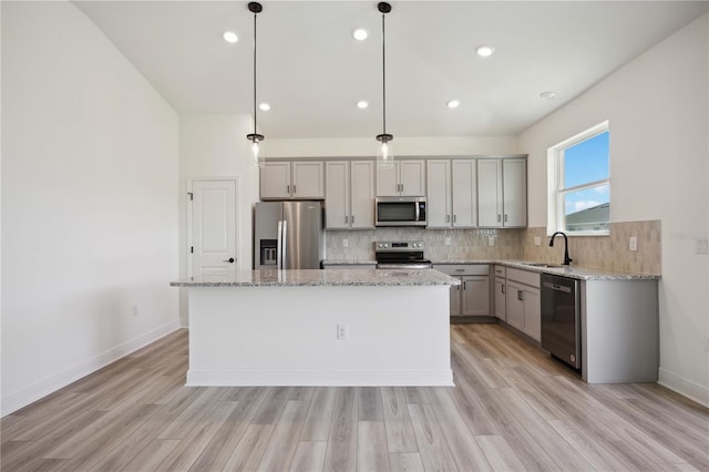 kitchen with gray cabinets, appliances with stainless steel finishes, hanging light fixtures, light stone counters, and a kitchen island