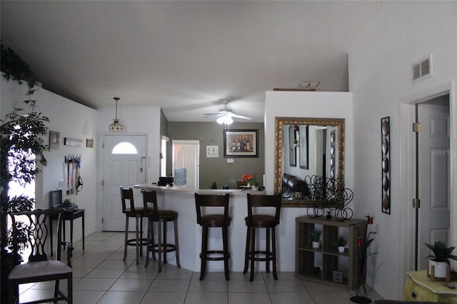 kitchen with a kitchen bar, ceiling fan, and light tile floors