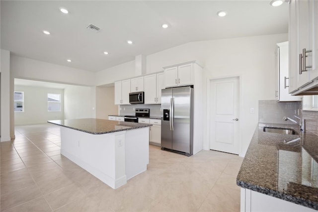 kitchen with appliances with stainless steel finishes, dark stone counters, sink, light tile patterned floors, and a kitchen island