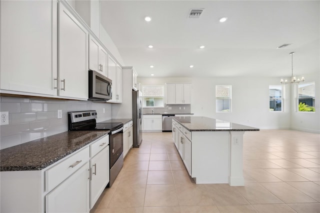 kitchen with appliances with stainless steel finishes, dark stone counters, light tile patterned floors, a center island, and white cabinetry