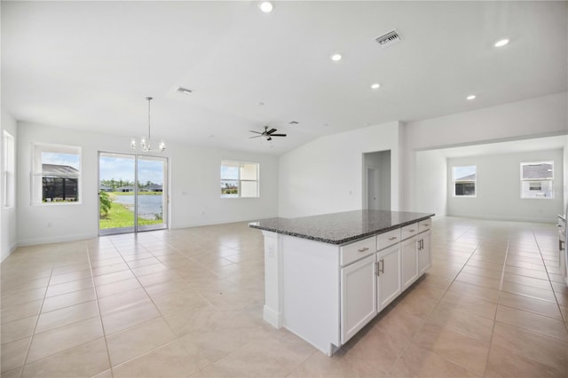 kitchen featuring dark stone counters, white cabinetry, ceiling fan with notable chandelier, a center island, and light tile patterned floors