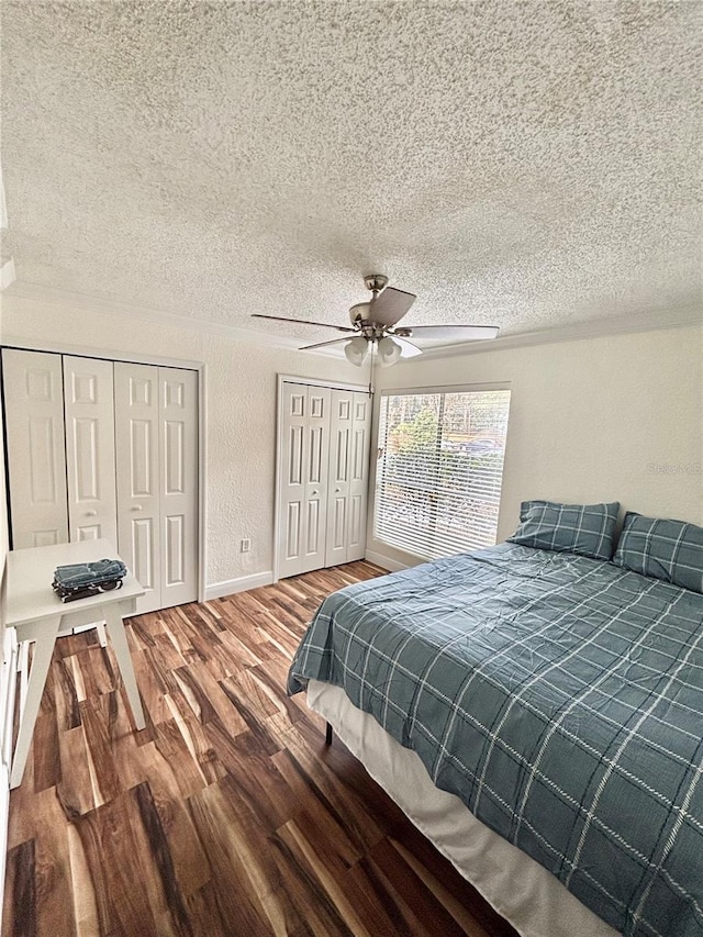 bedroom featuring hardwood / wood-style flooring, ceiling fan, multiple closets, and a textured ceiling