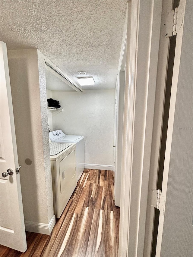 laundry room with wood-type flooring, washer and clothes dryer, and a textured ceiling