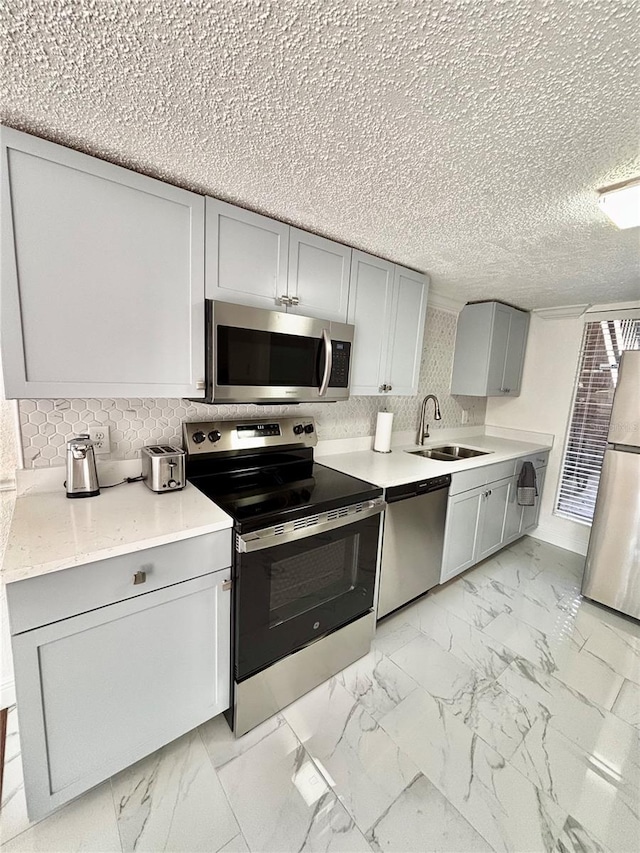 kitchen with sink, gray cabinetry, decorative backsplash, stainless steel appliances, and a textured ceiling