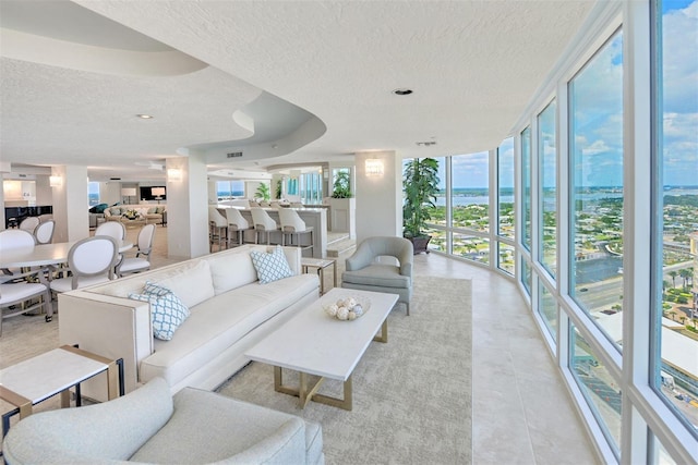 tiled living room featuring a raised ceiling, a water view, a textured ceiling, and a wall of windows