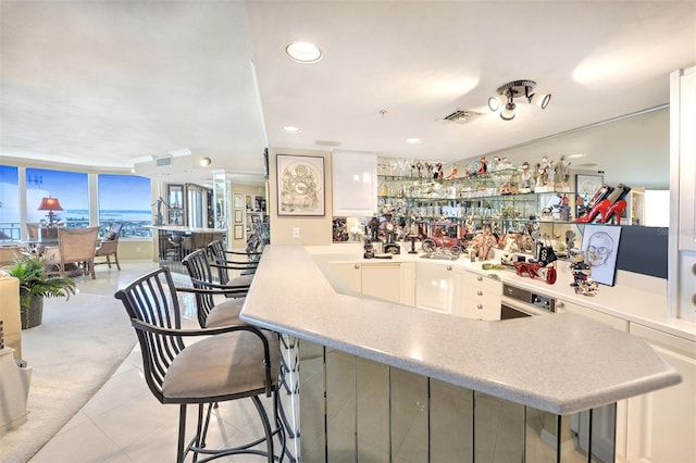 kitchen with a breakfast bar, kitchen peninsula, white cabinets, and light tile floors