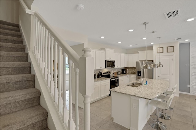 kitchen featuring stainless steel appliances, white cabinets, tasteful backsplash, and a kitchen island with sink