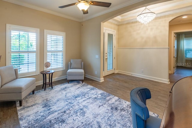 sitting room with ceiling fan with notable chandelier, wood-type flooring, and ornamental molding