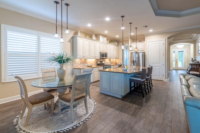 kitchen featuring appliances with stainless steel finishes, decorative backsplash, a kitchen island with sink, dark stone counters, and dark wood-type flooring