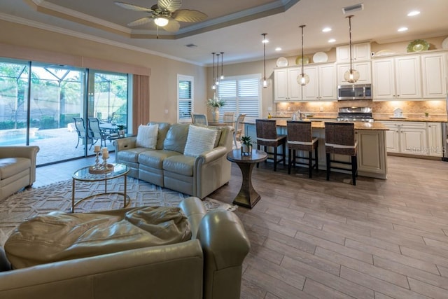 living room with ornamental molding, light hardwood / wood-style flooring, ceiling fan, and a tray ceiling