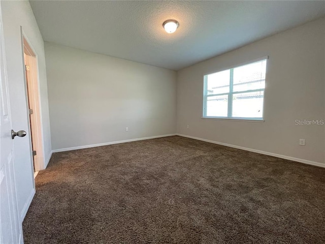 spare room featuring a textured ceiling and dark colored carpet