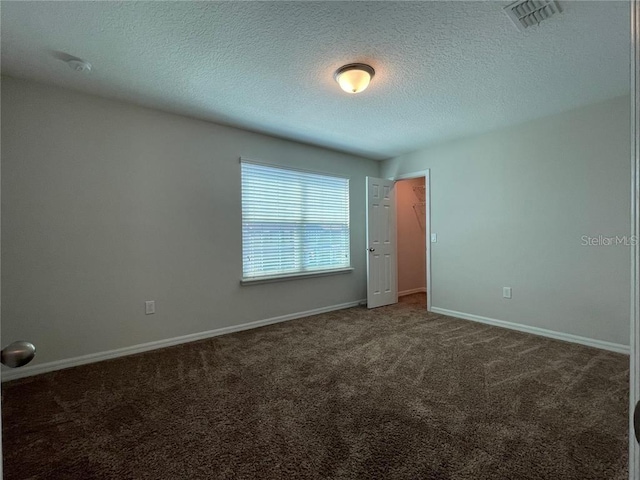 unfurnished room with a textured ceiling and dark colored carpet