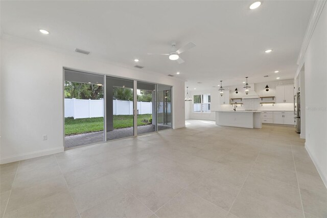 unfurnished living room with sink, crown molding, light tile patterned floors, and ceiling fan