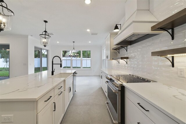 kitchen featuring an island with sink, white cabinetry, hanging light fixtures, electric range, and light stone counters