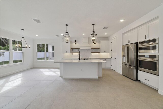 kitchen featuring pendant lighting, appliances with stainless steel finishes, a kitchen island with sink, a notable chandelier, and decorative backsplash