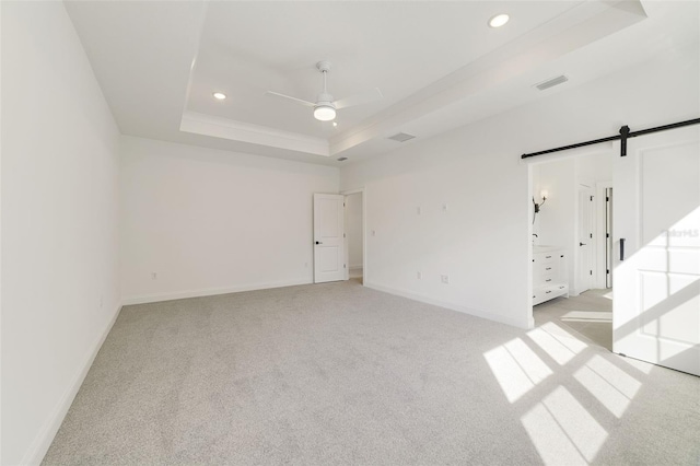 carpeted spare room with a barn door, ceiling fan, and a tray ceiling