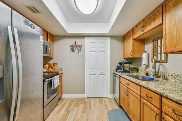 kitchen featuring stainless steel appliances, a raised ceiling, light stone countertops, light wood-type flooring, and sink