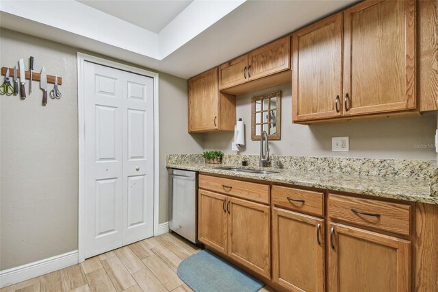 kitchen with light stone countertops, sink, light hardwood / wood-style floors, and stainless steel dishwasher