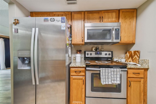 kitchen featuring stainless steel appliances, light stone counters, and hardwood / wood-style flooring